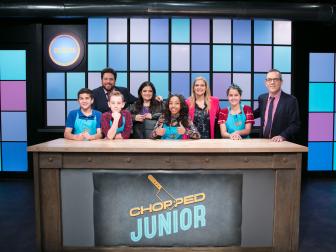 Judges and Junior contestants pose on set, from left to right, Matthew Merril, Scott Conant, Joshua Altamura, Alex Guarnaschelli, Kiara Roy, Amanda Freitag, Sophia Abreu, and Host Ted Allen during the appetizer round, as seen on Food Network's Chopped Junior, Season 6.