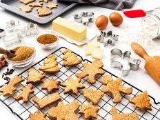Overhead view of a white background filled with ingredients for preparing Christmas cookies. A cooling rack and a baking sheet with fresh baked cookies complete the composition. High resolution 42Mp studio digital capture taken with SONY A7rII and Zeiss Batis 40mm F2.0 CF lens