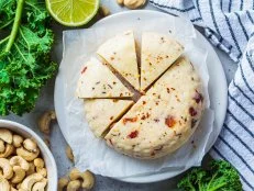 Vegan cashew cheese with dried tomatoes and spices on a white plate, gray background, top view. Alternative dairy-free diet, plant-based food.