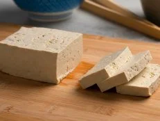 Piece of fresh raw organic tofu and slices on a cutting board close up