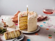 Homemade layered cake decorated with cheese cream icing and multi colored sugar sprinkles. Beautiful birthday cake with candle on a table.