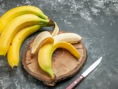 Top view nutrition source fresh bananas bundle and peeled on wooden cutting board knife on gray background