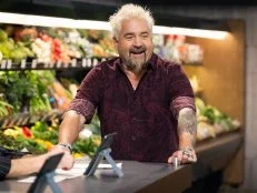 Host Guy Fieri welcomes the judges, as seen on Guy's Grocery Games, Season 39, in front of a produce display.