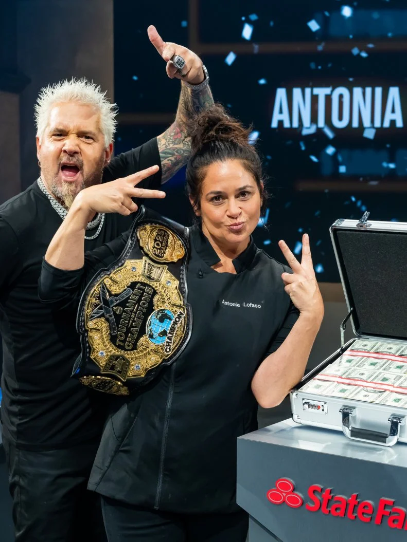 Host Guy Fieri and winning contestant Antonia Lofaso pose with the Championship belt and briefcase with winning prize of $150,000 sponsored by StateFarm, as seen on Tournament of Champions, Season 6.