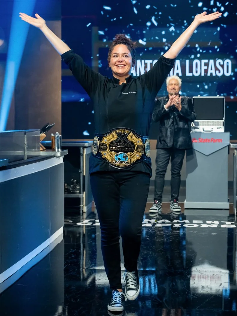 Host Guy Fieri and contestant Antonia Lofaso react as she is announced the winner of Tournament of Champions and given the Championship belt, as seen on Tournament of Champions, Season 6.
