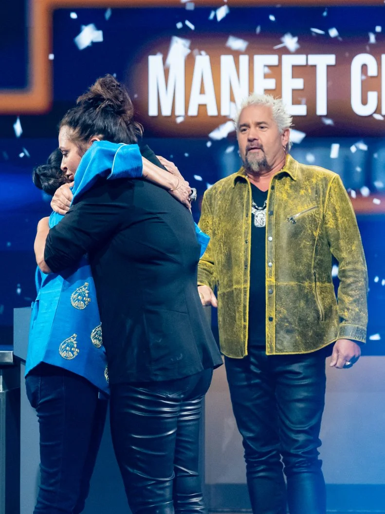 Contestant Antonia Lofaso congratulates Maneet Chauhan for winning the 2024 Tournament of Champions, alongside Host Guy Fieri, as seen on Tournament of Champions, Season 5.