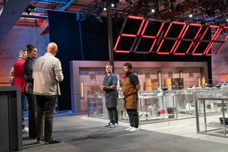 Chef Bryan Voltaggio and Chef Jonathon Sawyer stand before the judges for their verdict; Host Michael Symon, Judges Antonia Lofaso, Graham Elliot, Jet Tila, and Host Esther Choi, as seen on 24 in 24: Last Chef Standing, Season 2.
