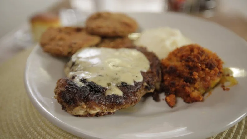 The main component of this meat and three plate from Arnold's Country Kitchen is the breaded & flat-top cooked pork chop coated in white gravy, as seen on Bizarre Foods Delicious Destinations.