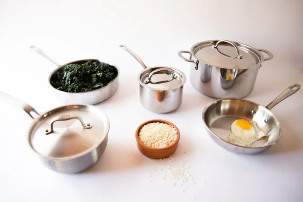 Five pieces of stainless steel cookware arranged on a white countertop