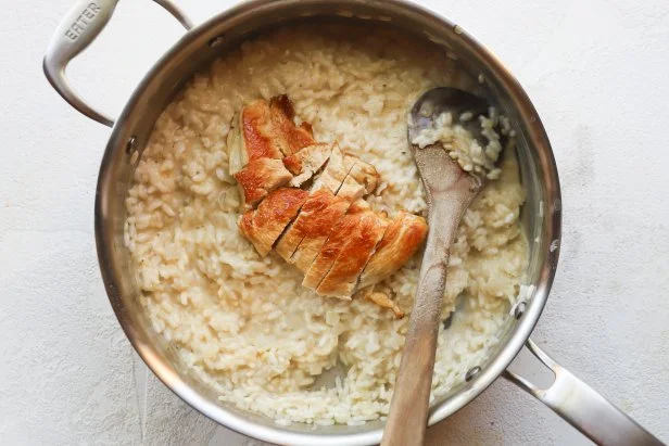 Seared chicken breast on top of cooked risotto in stainless steel pan